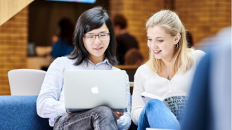 Two female students are looking at a laptop.