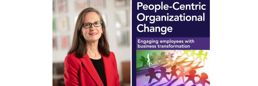 Business headshot of Julie Hodges in red suit in the Business School lounge next to an image of her new book, 'People-centric organizational change'