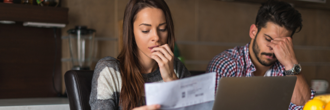 Worried heterosexual, caucasian couple sitting in the kitchen looking at bills