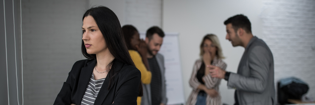 Woman in foreground with group of people gossiping in the background of an office