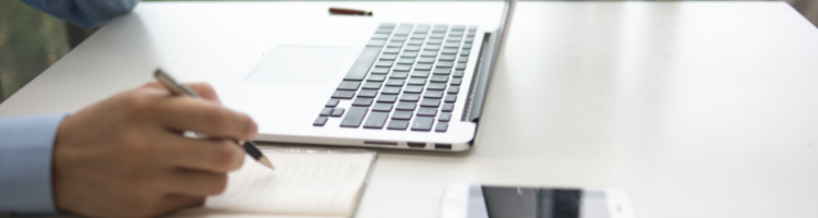 Hand writing on pad with a laptop on a desk