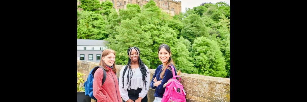 Three female students standing on a bridge, with Castle in background