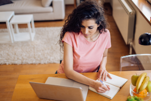 Girl writing while looking at a laptop