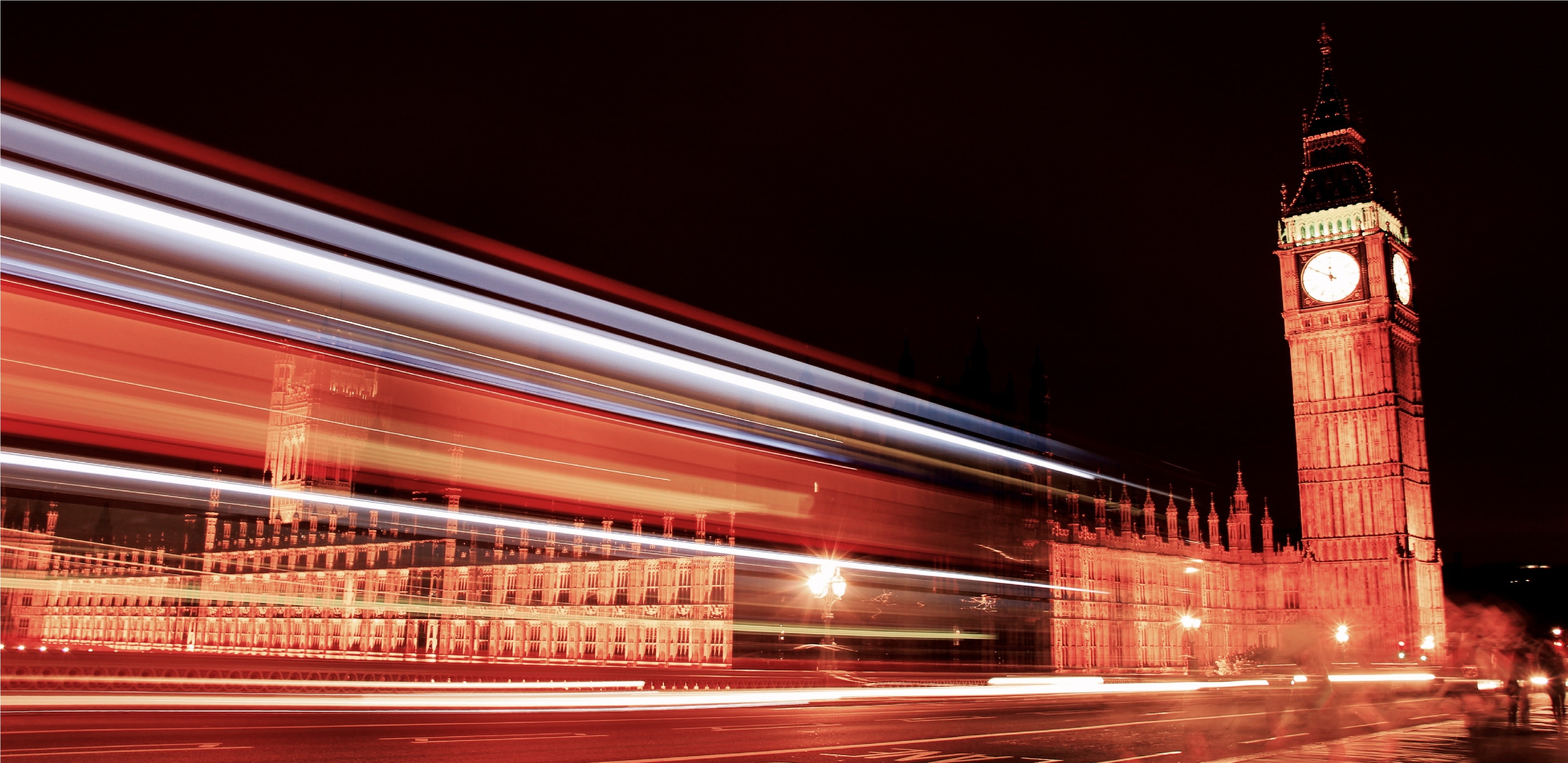 Big Ben and the Houses of Parliament at night, partially obscured by lines of colour from the speed of a double decker bus.