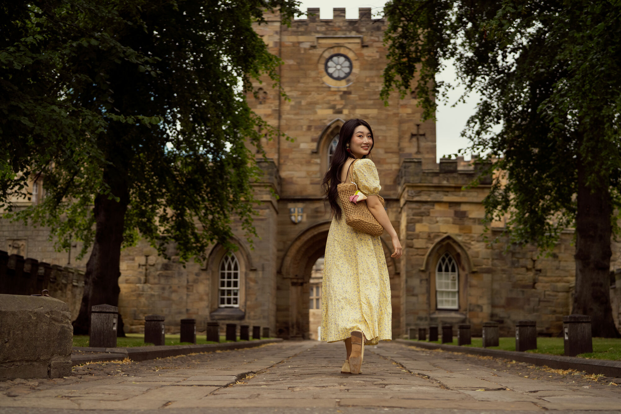 TA student walking towards Durham Castle, looking back over her shoulder and smiling.