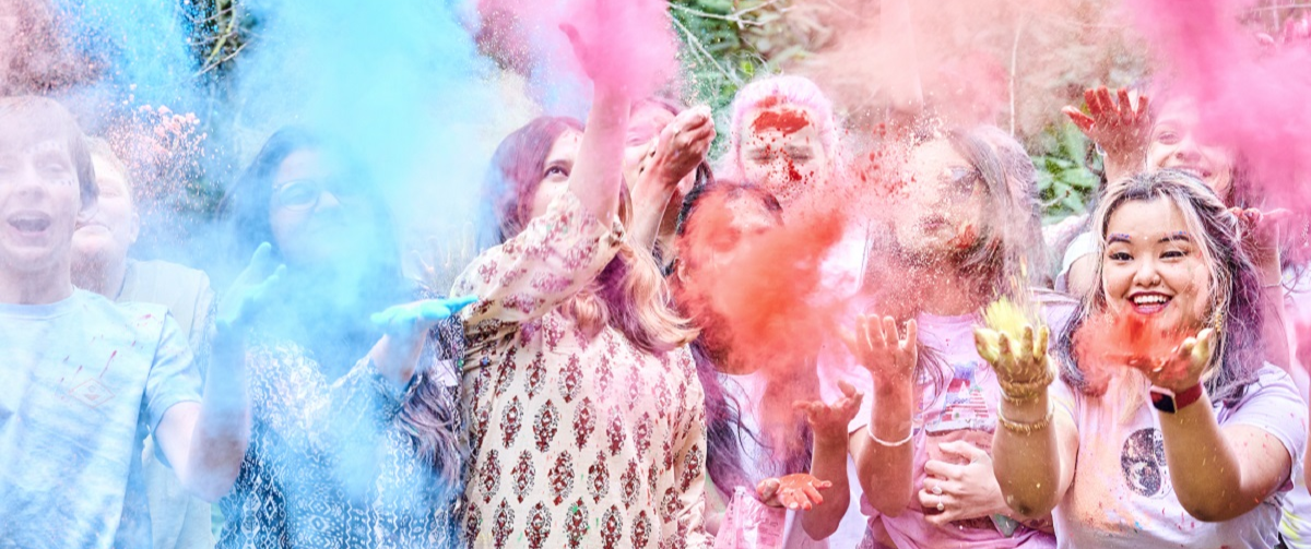 A group of students and members of the public throwing brightly coloured powder to celebrate the Indian Holi festival