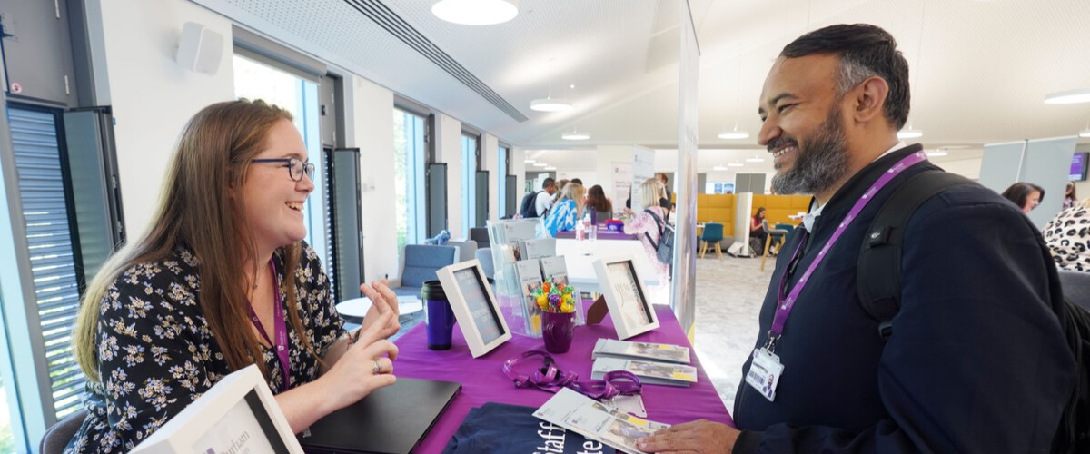 Staff talk to each other in front of pop up banner and tables covered with information leaflets about staff volunteering