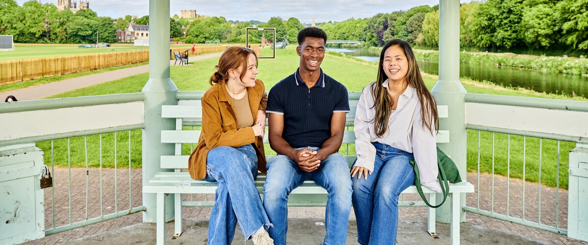 a diverse group of students sitting on a bench in front of a playing field