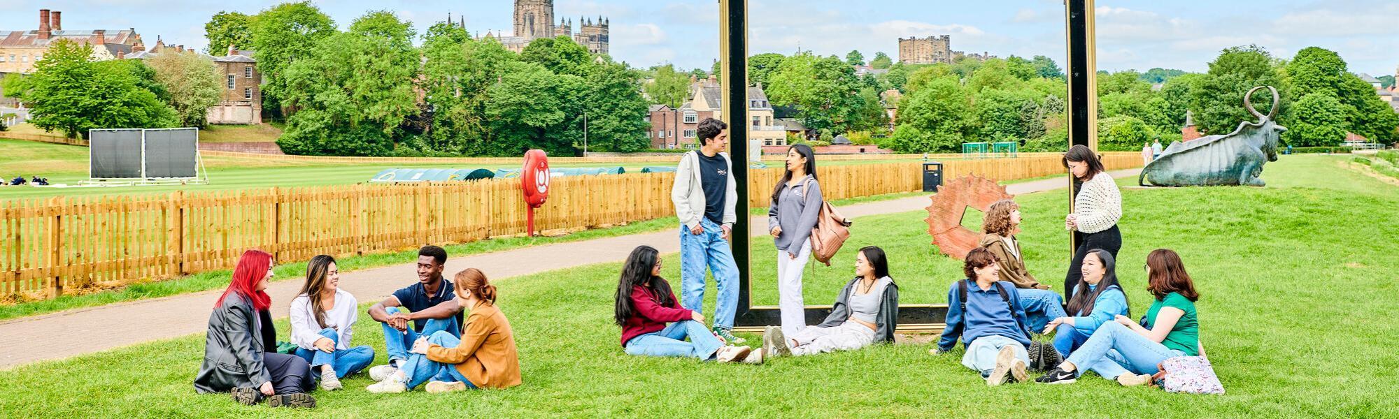 Groups of students sitting and standing on grass with Durham Cathedral in the background