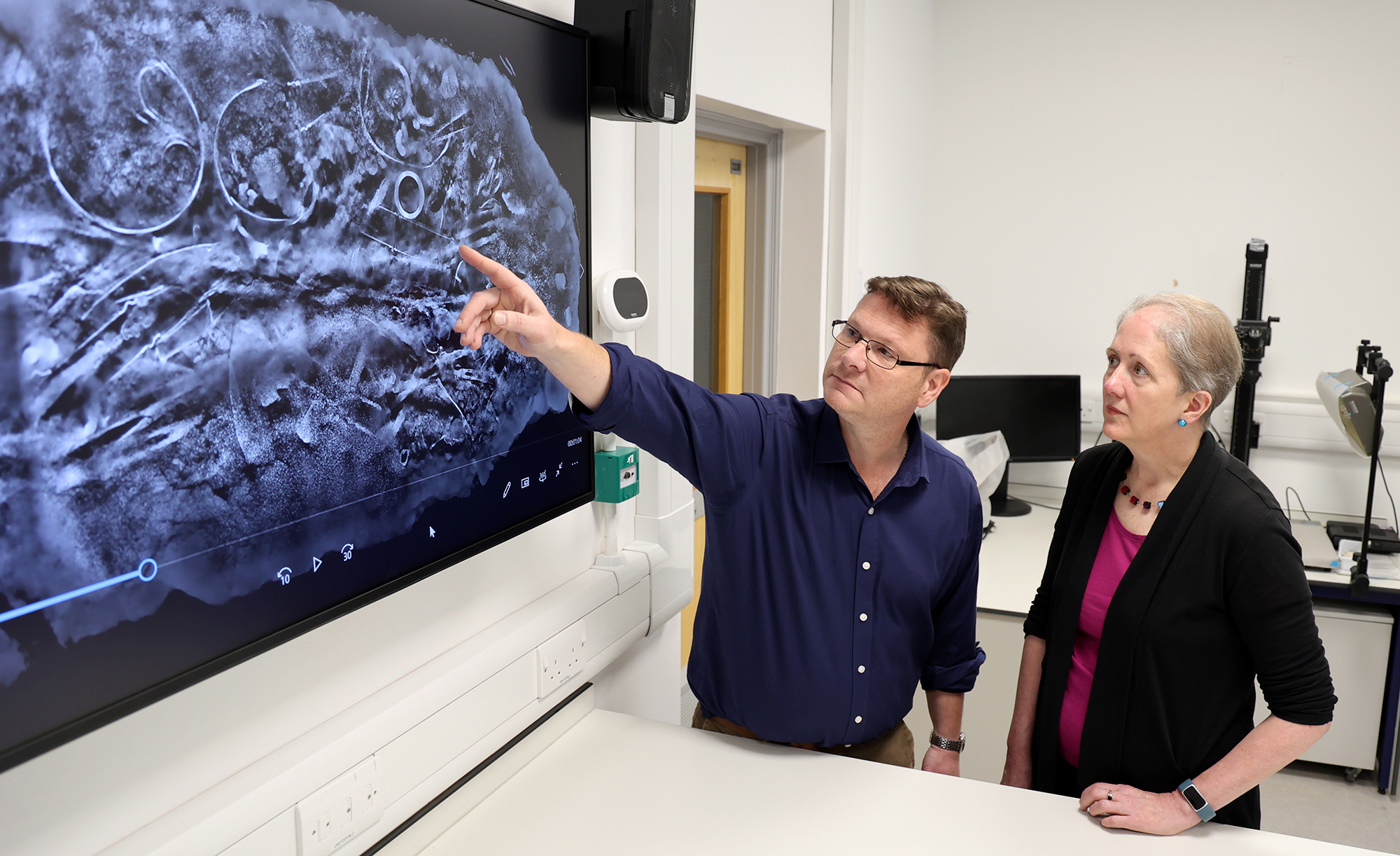 Two people looking at a CT scan, produced by MUVIS, University of Southampton, of the block of artefacts excavated from Melsonby. From left to right: Professor Tom Moore, Head of the Department of Archaeology, and Dr Emily Williams, Department of Archaeology.