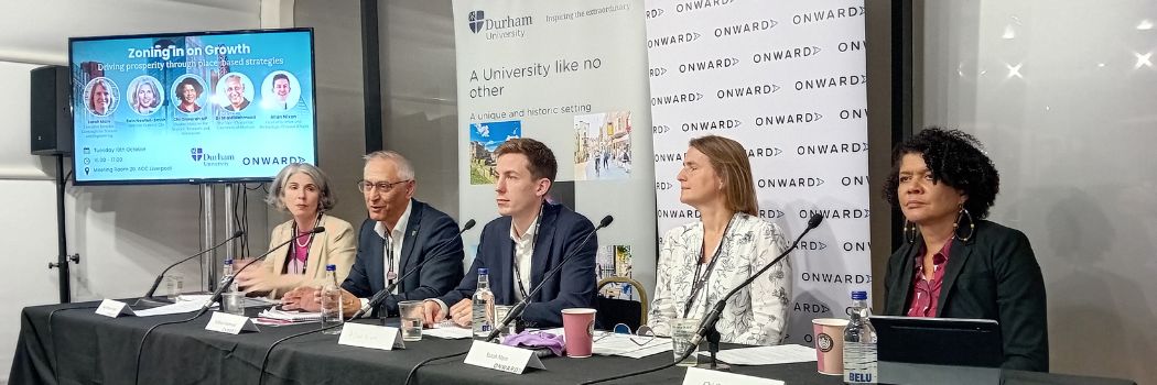 Five people sitting behind a table, with the man second left addressing the audience (off camera)