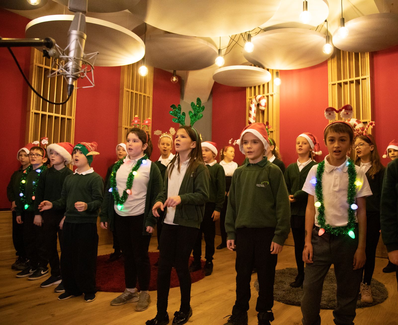 A group of children singing in the recording studio at Collingwood, wearing Christmas accessories