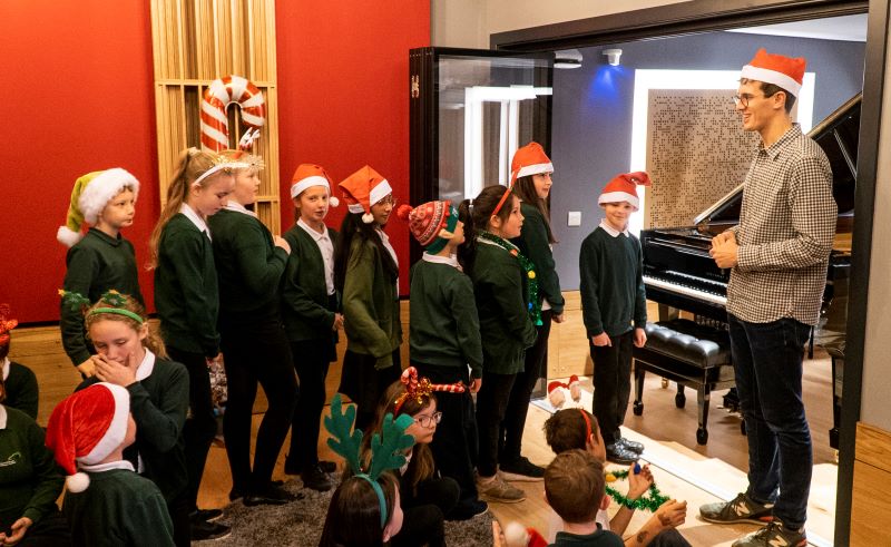 Children dressed in Christmas accessories queue up to play a Steinway piano