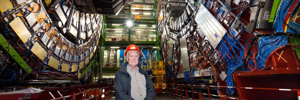 Peter Higgs standing in front of the Large Hadron Collider at CERN where the Higgs boson he theorised was discovered.