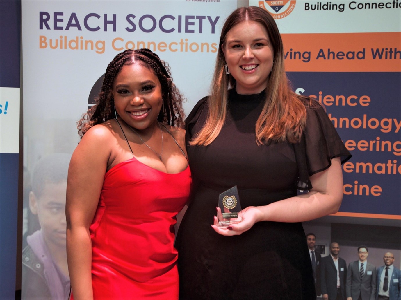 A student in a red dress with a member of staff wearing black, receiving the Reach Society Award