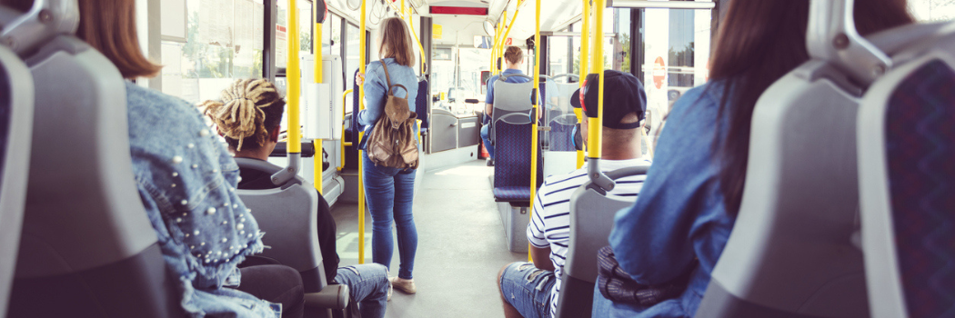 The inside of a bus; passengers are sitting on seats and standing holding the rail