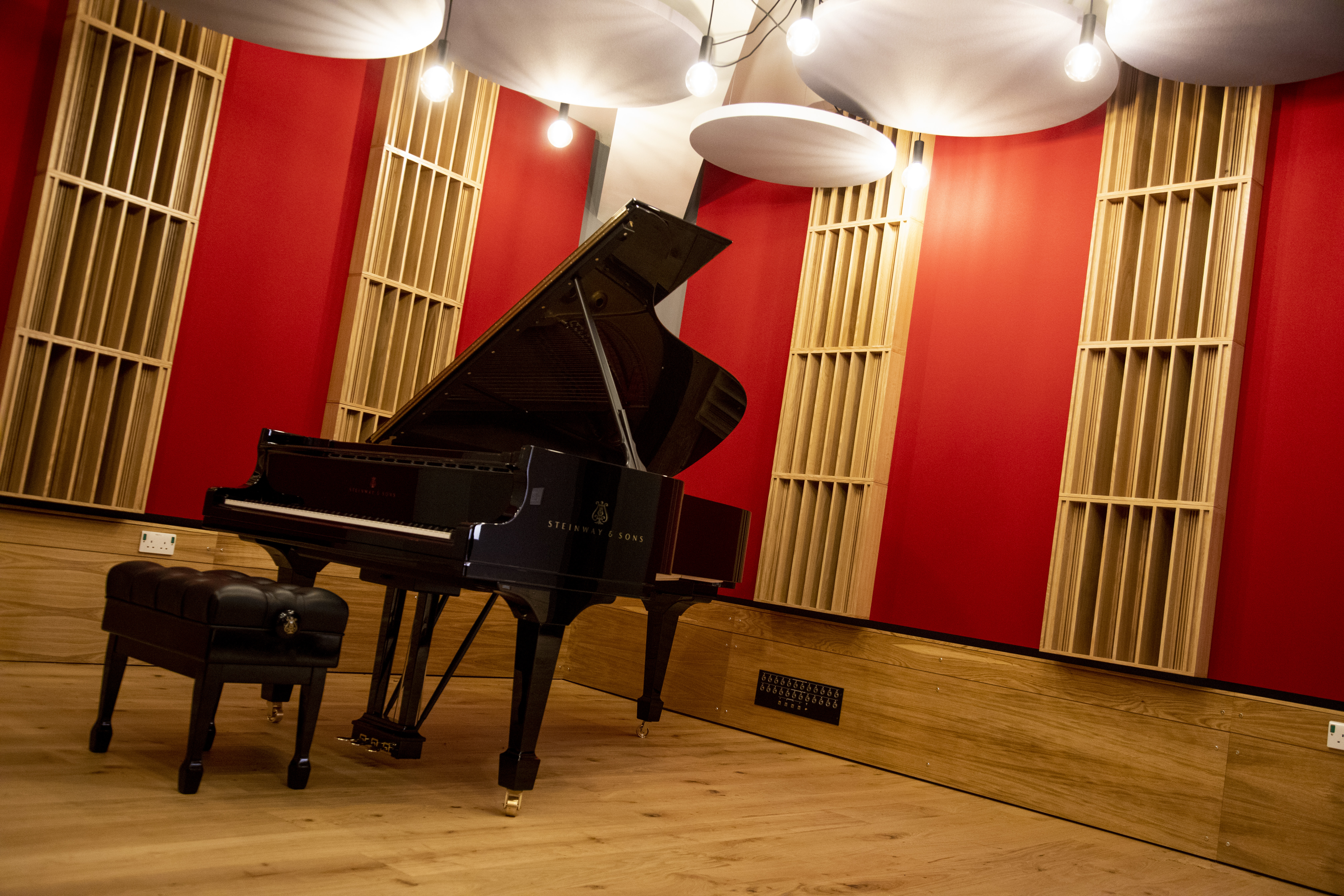a grand piano in a music room with red and grey acoustic panels