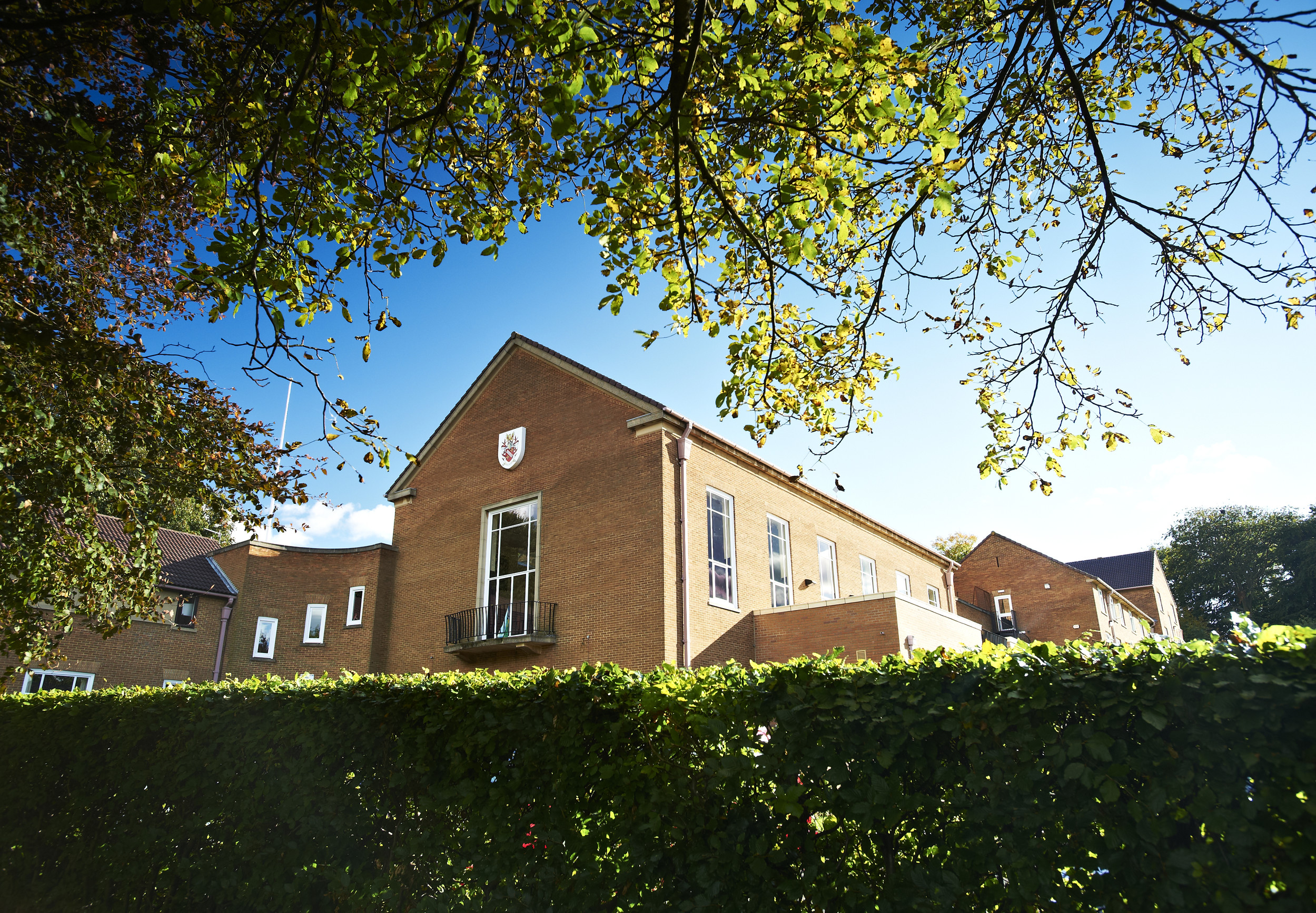 Exterior of  a Grey College building behind a hedge