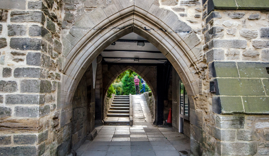 TThe college grounds chapel archway, people stand talking on the other side