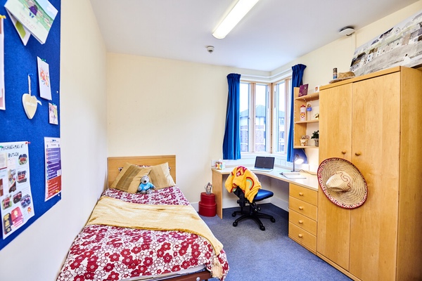 An image of a bedroom with bed, desk, and wardrobe