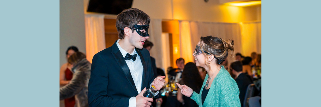 A male and female student wearing masks and in evening attire facing each other talking