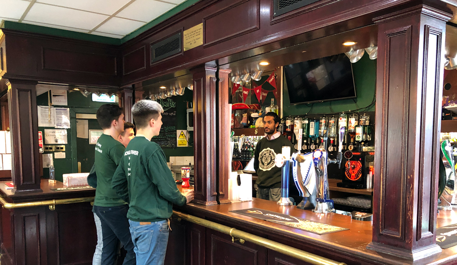 Traditional wooden bar with students ordering drinks.