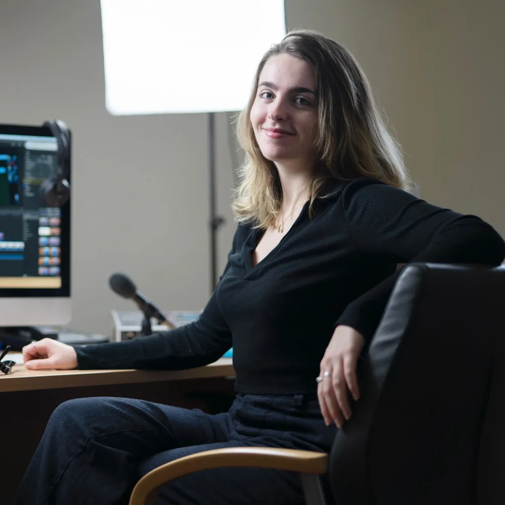 A young woman sits at a desk back lit