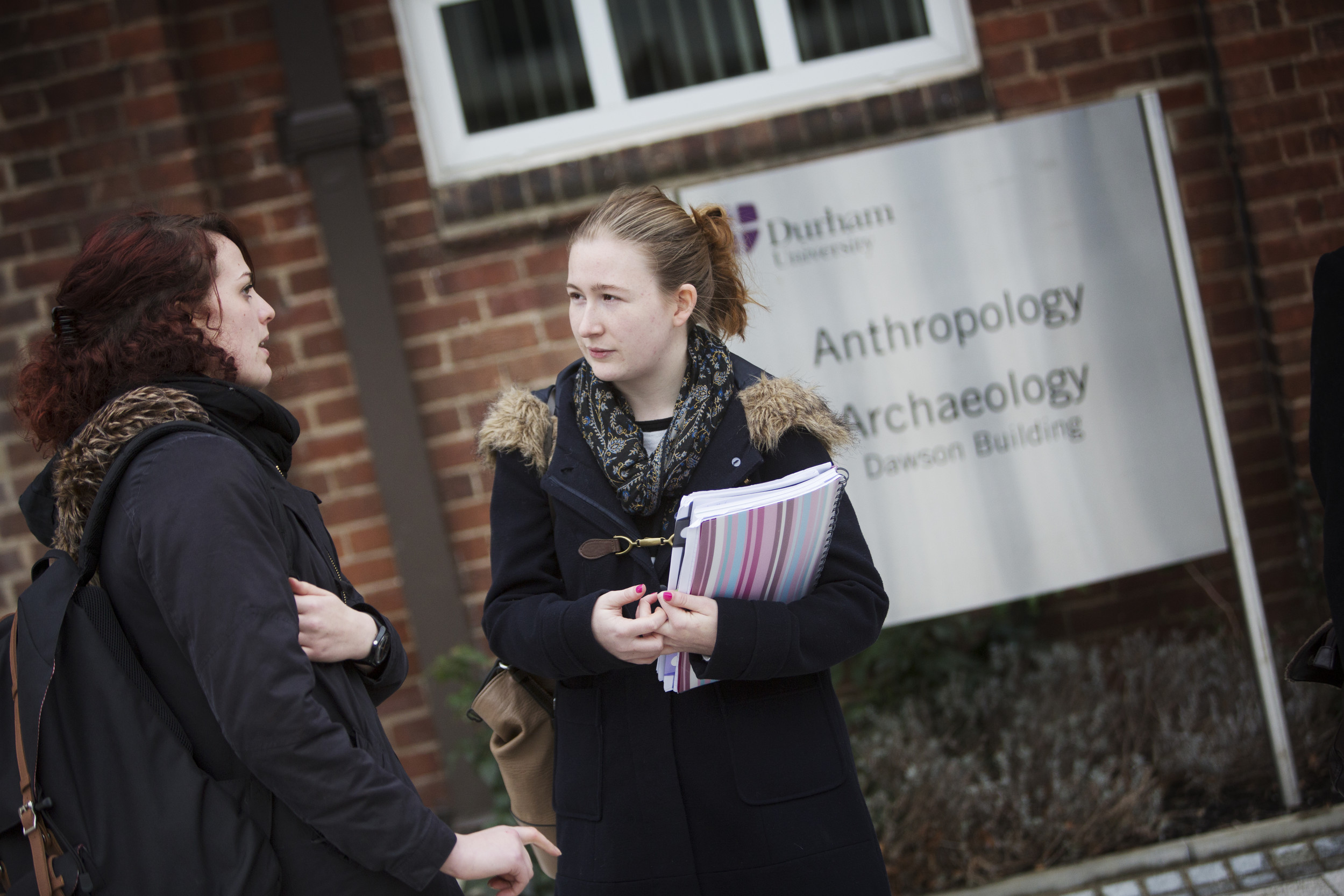 Two students chatting in front of the anthropology sign