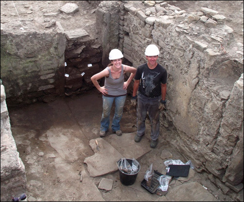 Two archaeologists standing within a room of an excavated building
