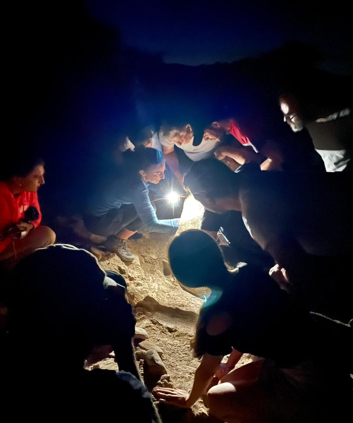 Archaeologists and Cañaveral de León community members jointly lift Stela 2 at night time, illuminated by flashlights.