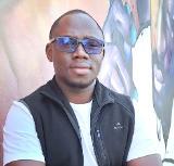 An early career researcher, Lamine Badji, wearing a white T-shirt, black fleece gilet and glasses, smiling at the camera.