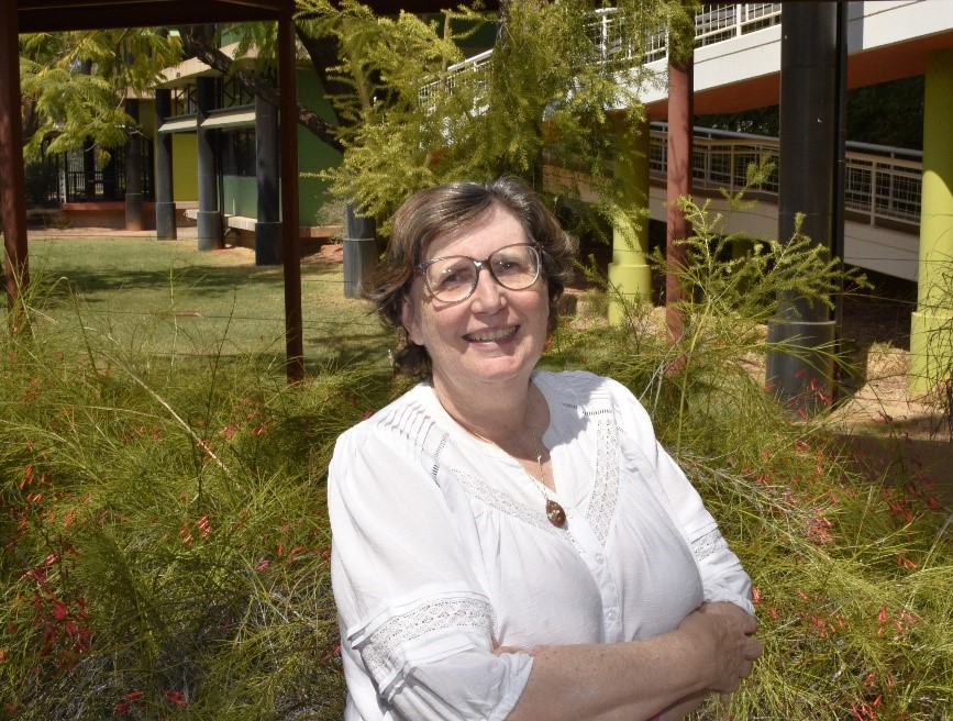 A photo of Dr Felicity McLure, standing arms crossed in front of a bush