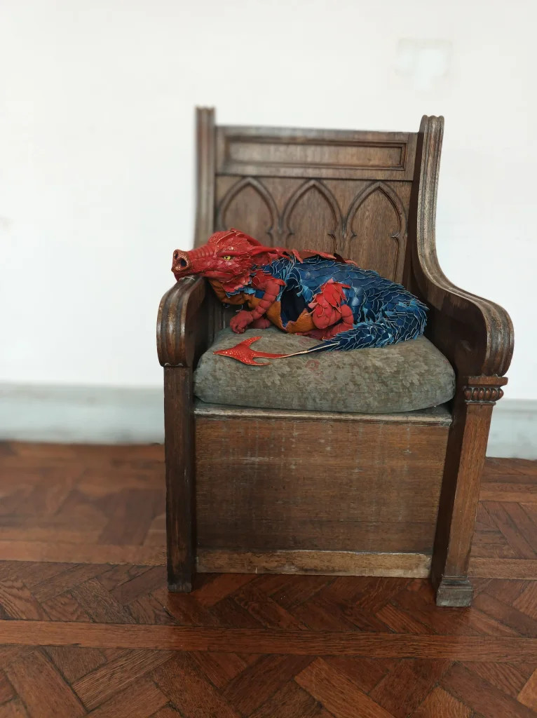 Photograph of a red and blue dragon puppet curled in a wooden throne