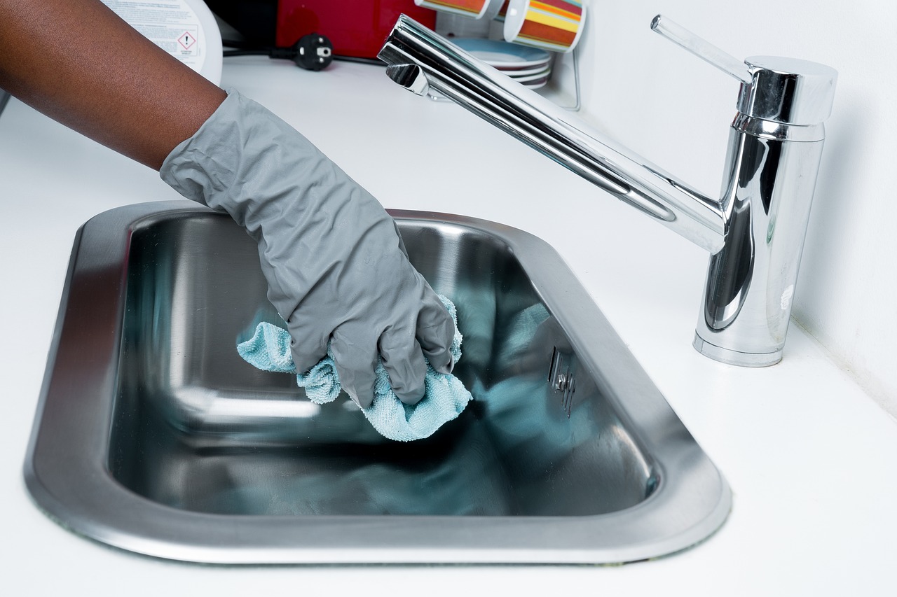 A person wearing a plastic glove cleaning a spotless sink
