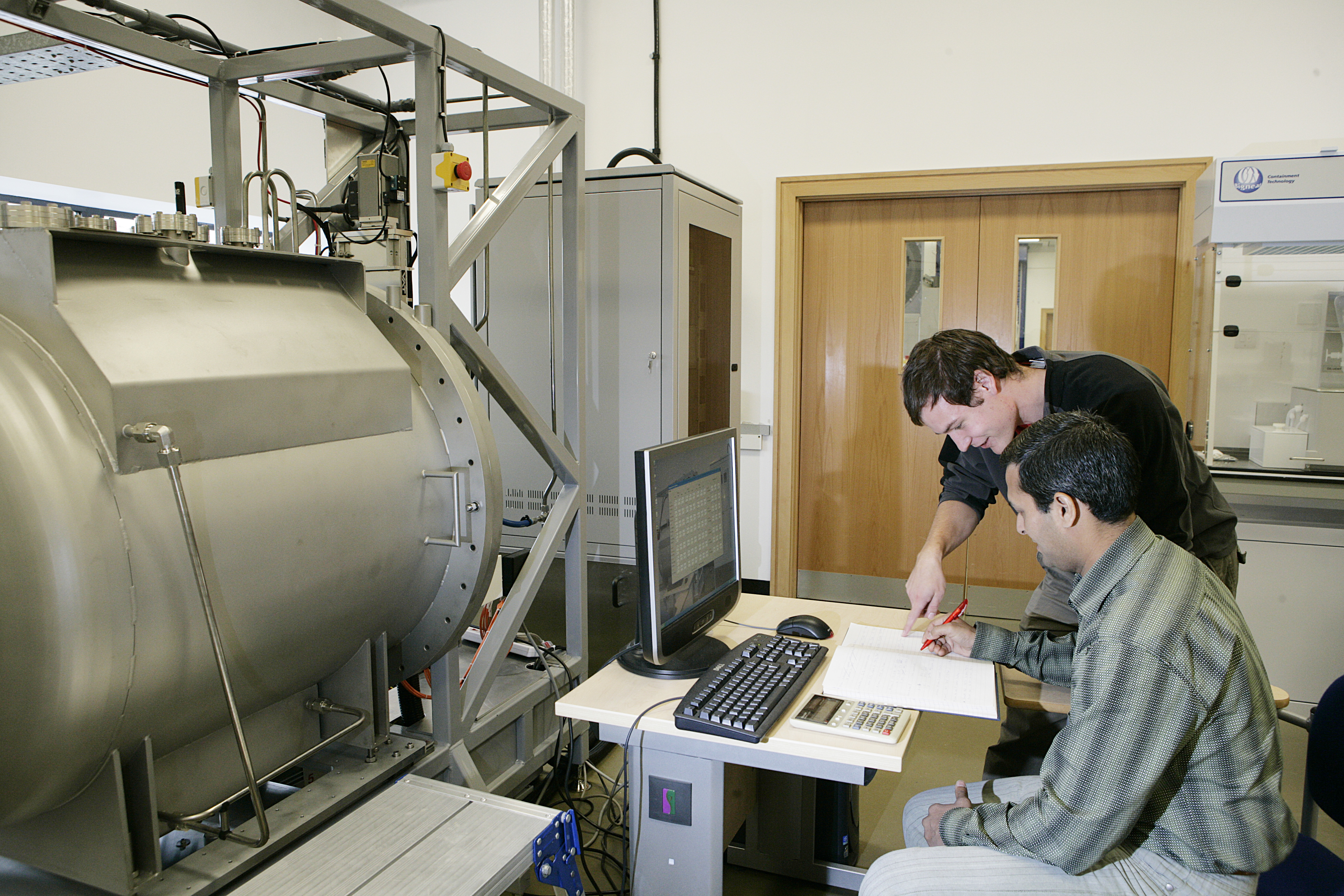 Image of two people making notes alongside the large lab equipment at NETpark