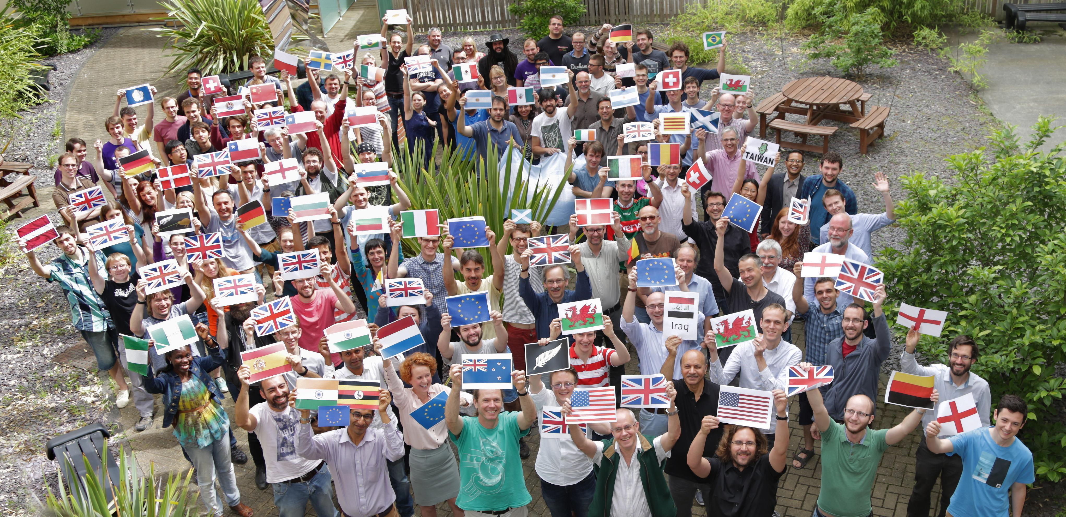 Big group photo of our many international staff and students holding up the flags of the countires they are from.