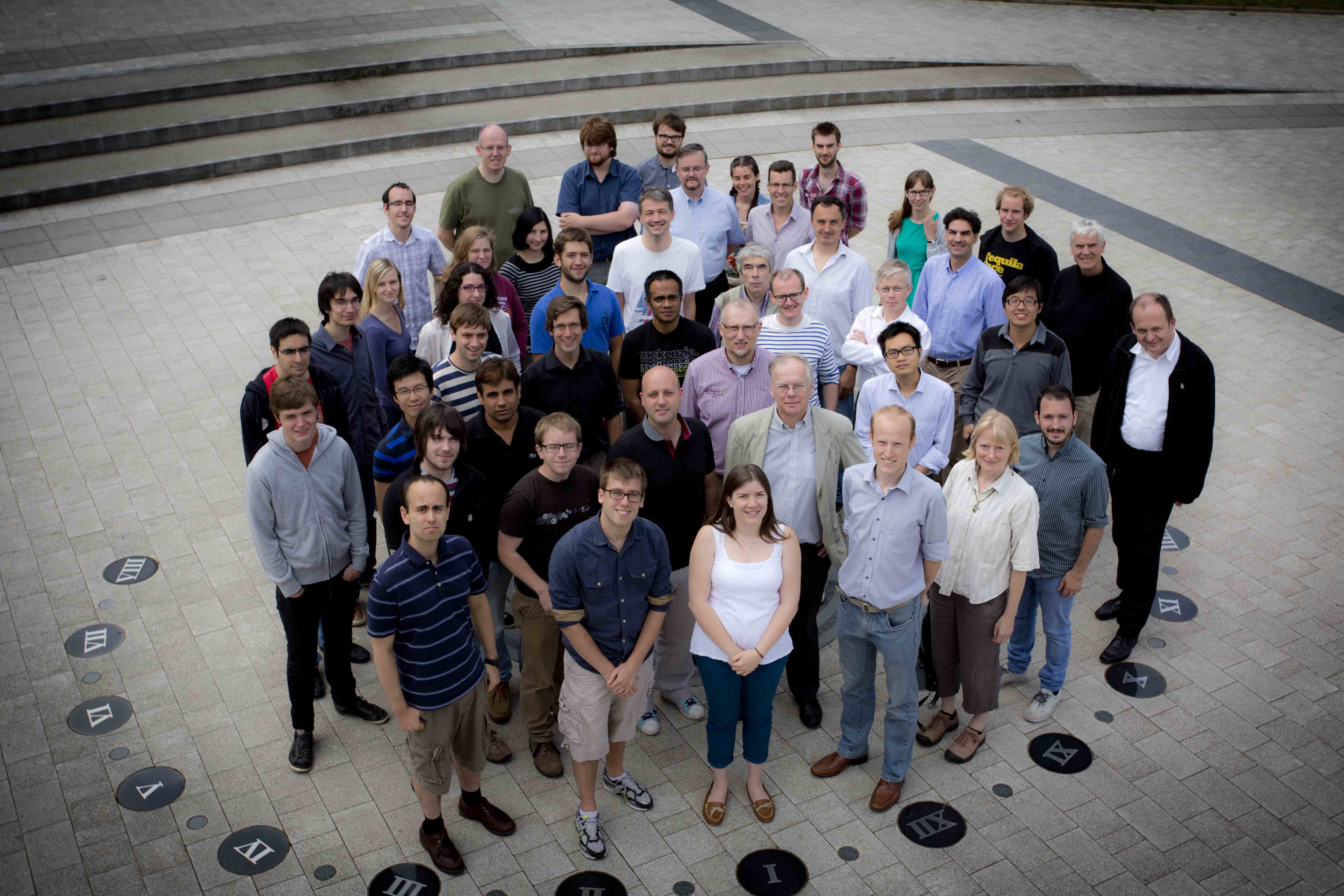 Group of postgraduate students and staff from the Joint Quantum Centre, gathered outside the Rochester Building, stood inside our sundial feature in the pavement with their supervisor Robert Potvliege