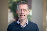 Man with grey hair and glasses smiles at the camera