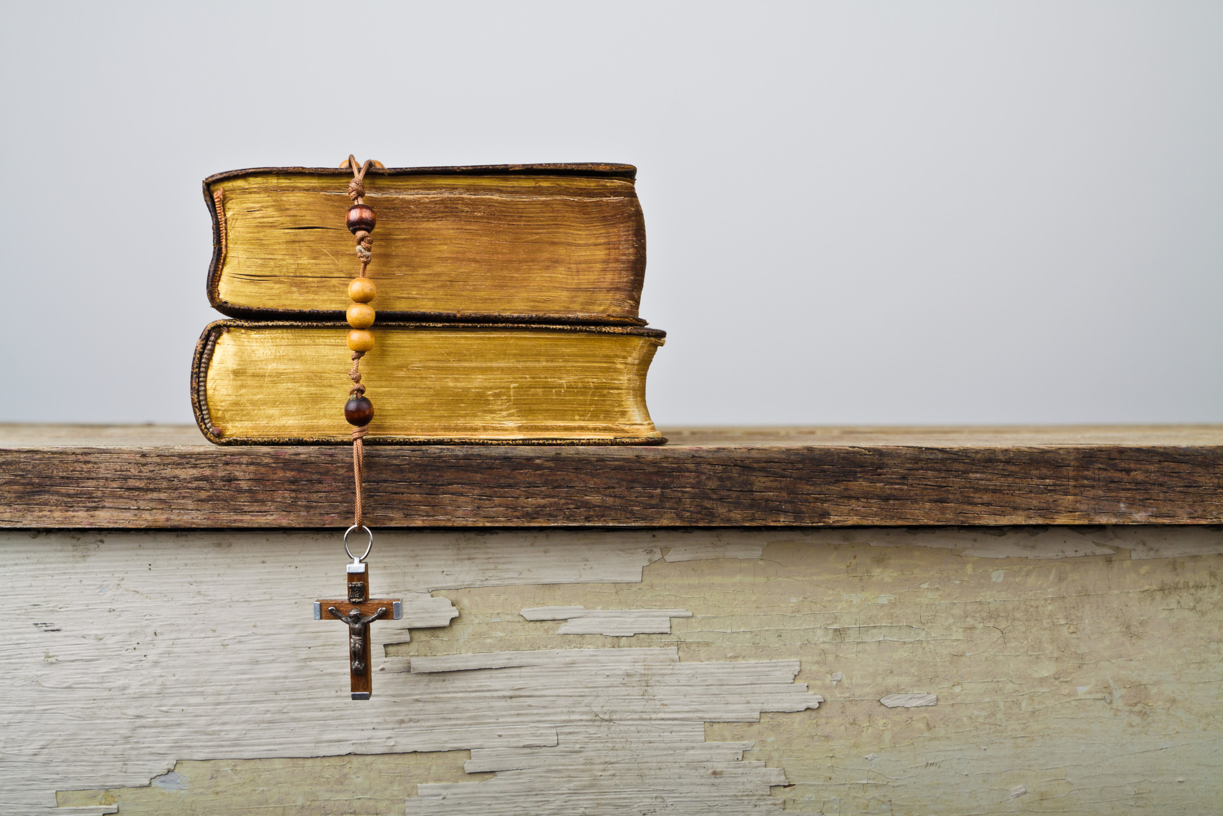 A pile of two books, with rosary beads and a cross