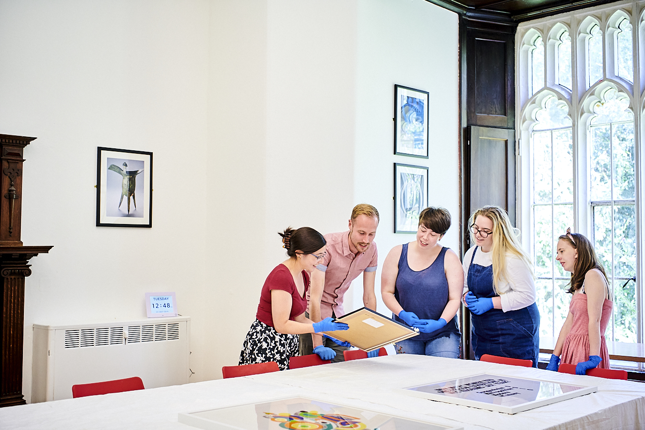 A group of people wearing gloves gather round as a woman shows them a framed picture.