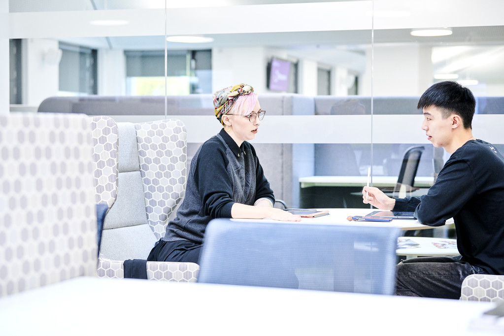 A woman with pink hair talking with a man at a table