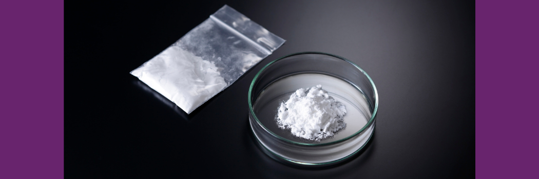 White powder in a dish and in a small plastic bag sit on a black surface