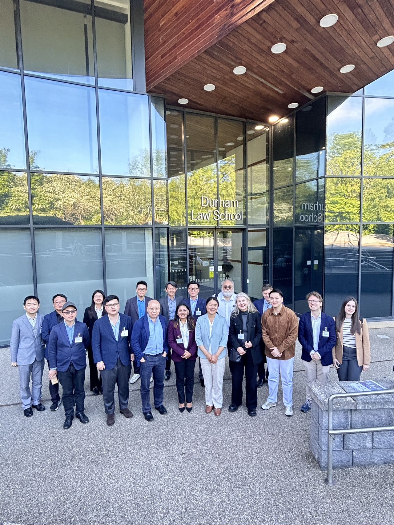 A group photo of international participants of a conference in front of a glass building of the Durham Law School.