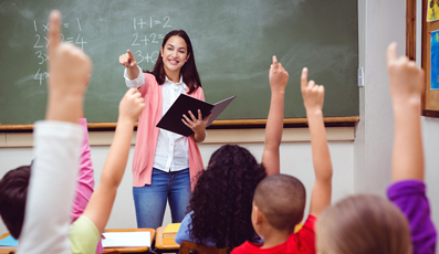 A classroom full of children holding their hands up to answer a question