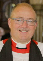 A man with grey hair and glasses wearing a clerical collar