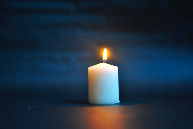 A lit white candle against a dark blue background