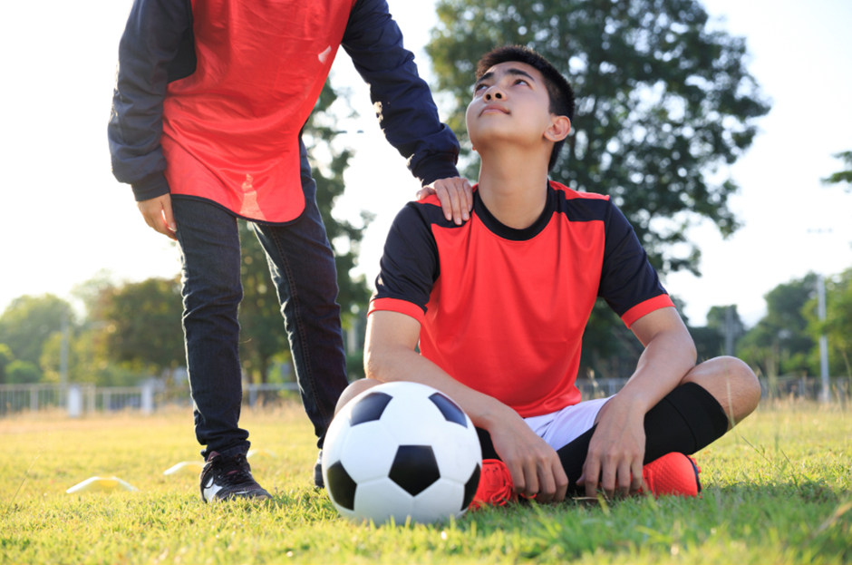 A student sat on a football putch with a ball infront