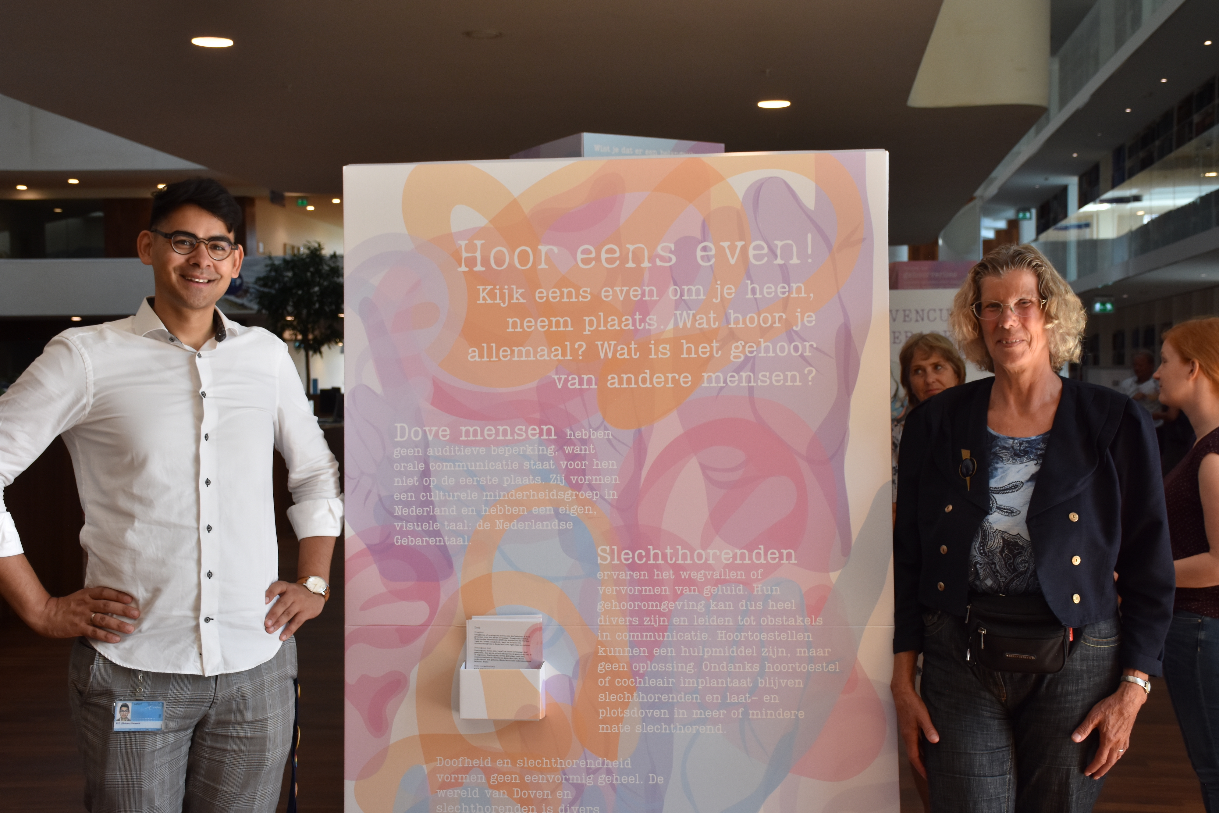 Two people stood at either side of the 'Yo, Doc, Listen Up!' exhibition poster