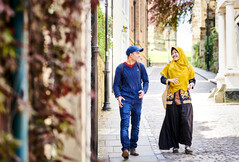 male student with blue cap and female student with yellow head dress walking along street