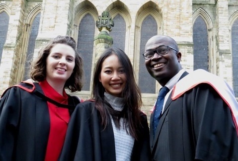 Three students wearing graduation gowns outside Durham Cathedral